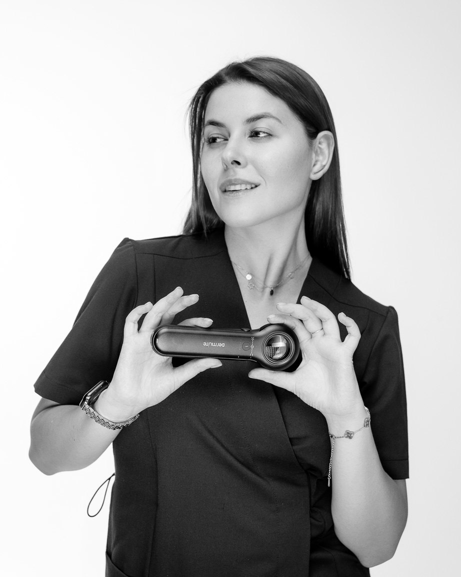 Yulia Agranovych in medical scrubs holding a dermatoscope, black-and-white photograph