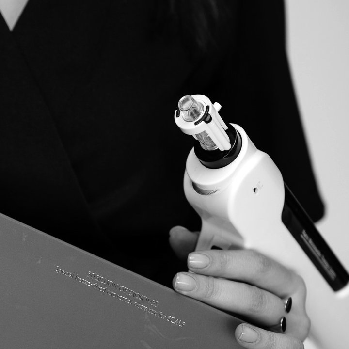 A doctor’s hands holding a scalp mesotherapy device, black-and-white photograph